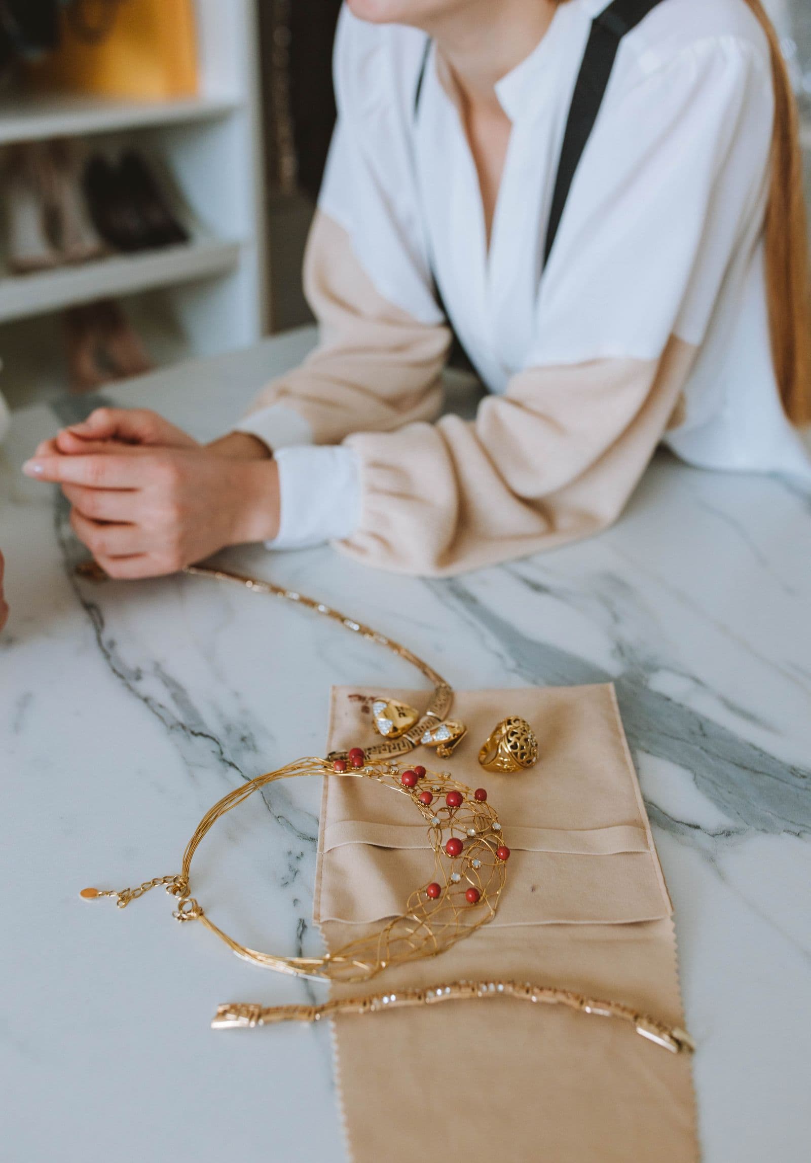 A gold necklace, ring and bracelet laid out on a suede pouch on a marble counter.