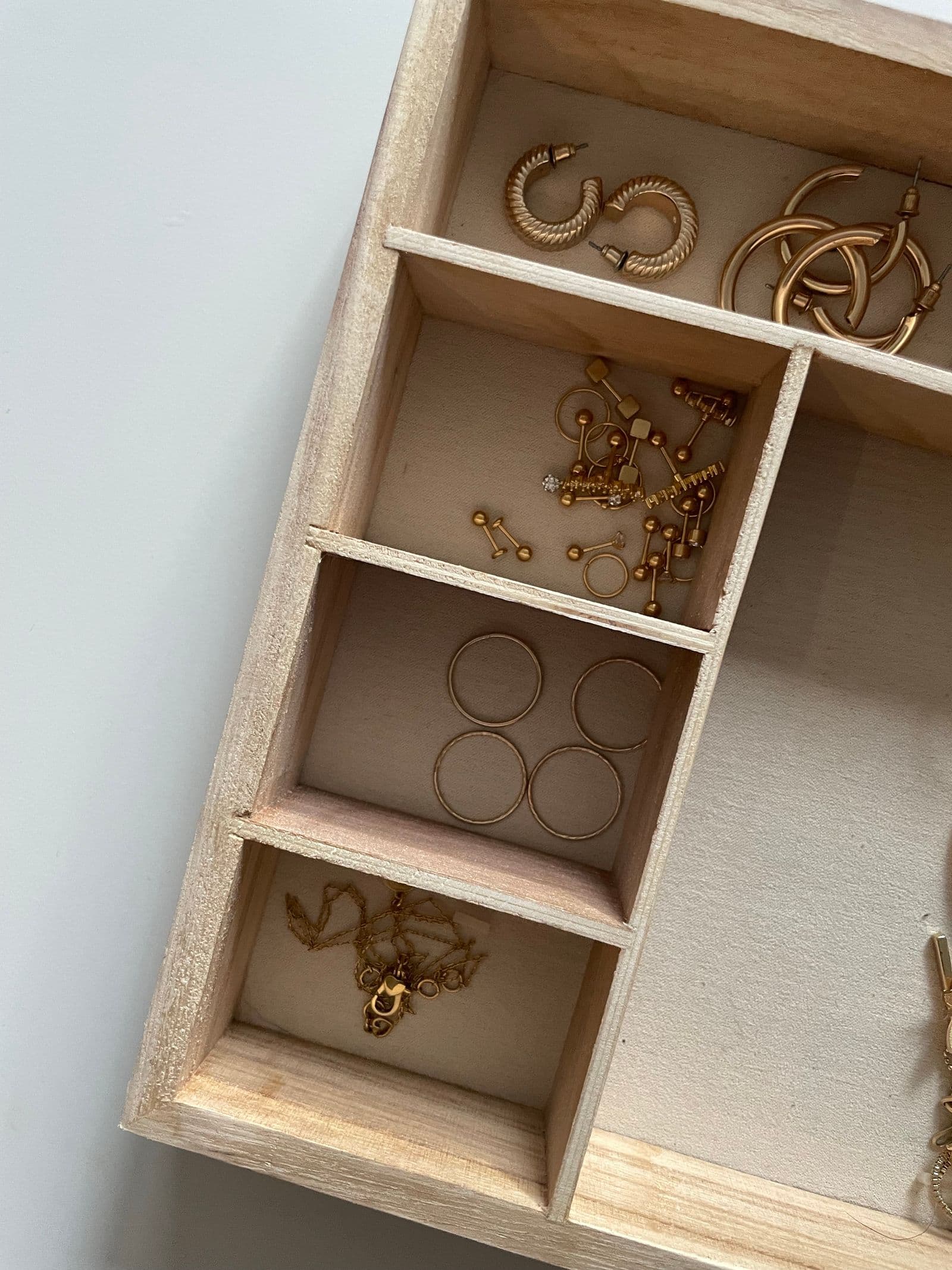 A compartmented wooden tray holding hoops, studs, plain bands and a folded chain.