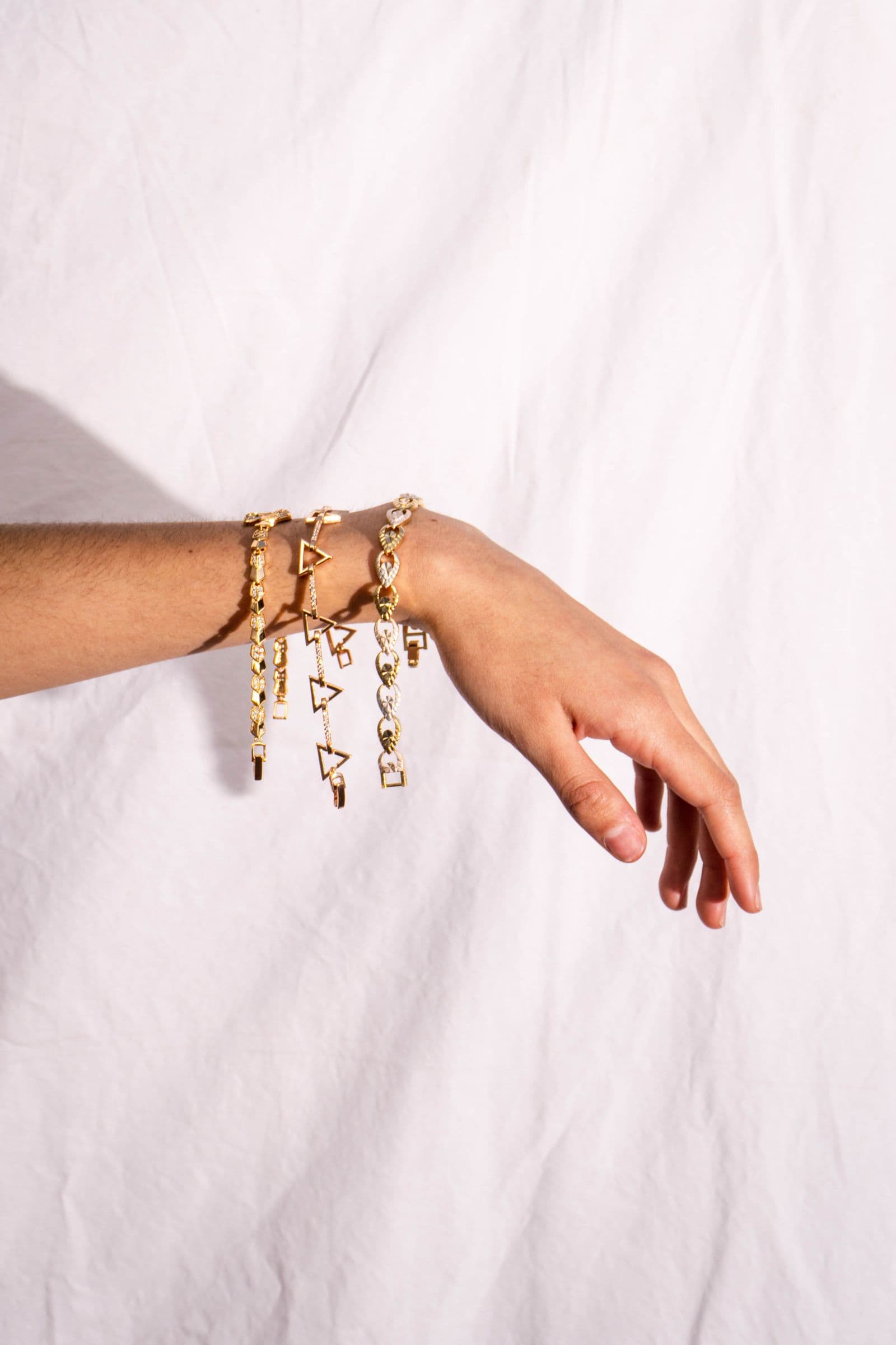 Three slim gold chain bracelets on a bare wrist against white cloth.
