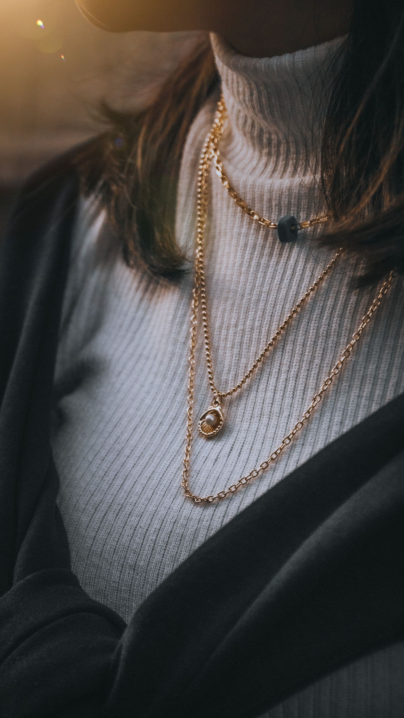 Three gold chains worn at three different lengths over a cream ribbed polo neck.