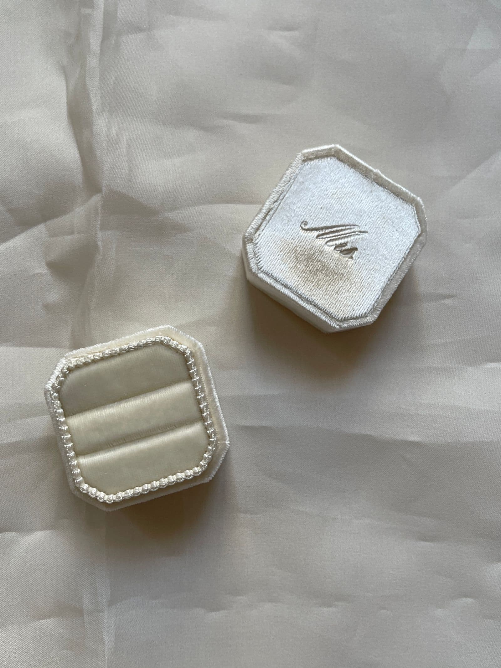 Two ivory velvet ring boxes, one open and one closed, on cream silk.