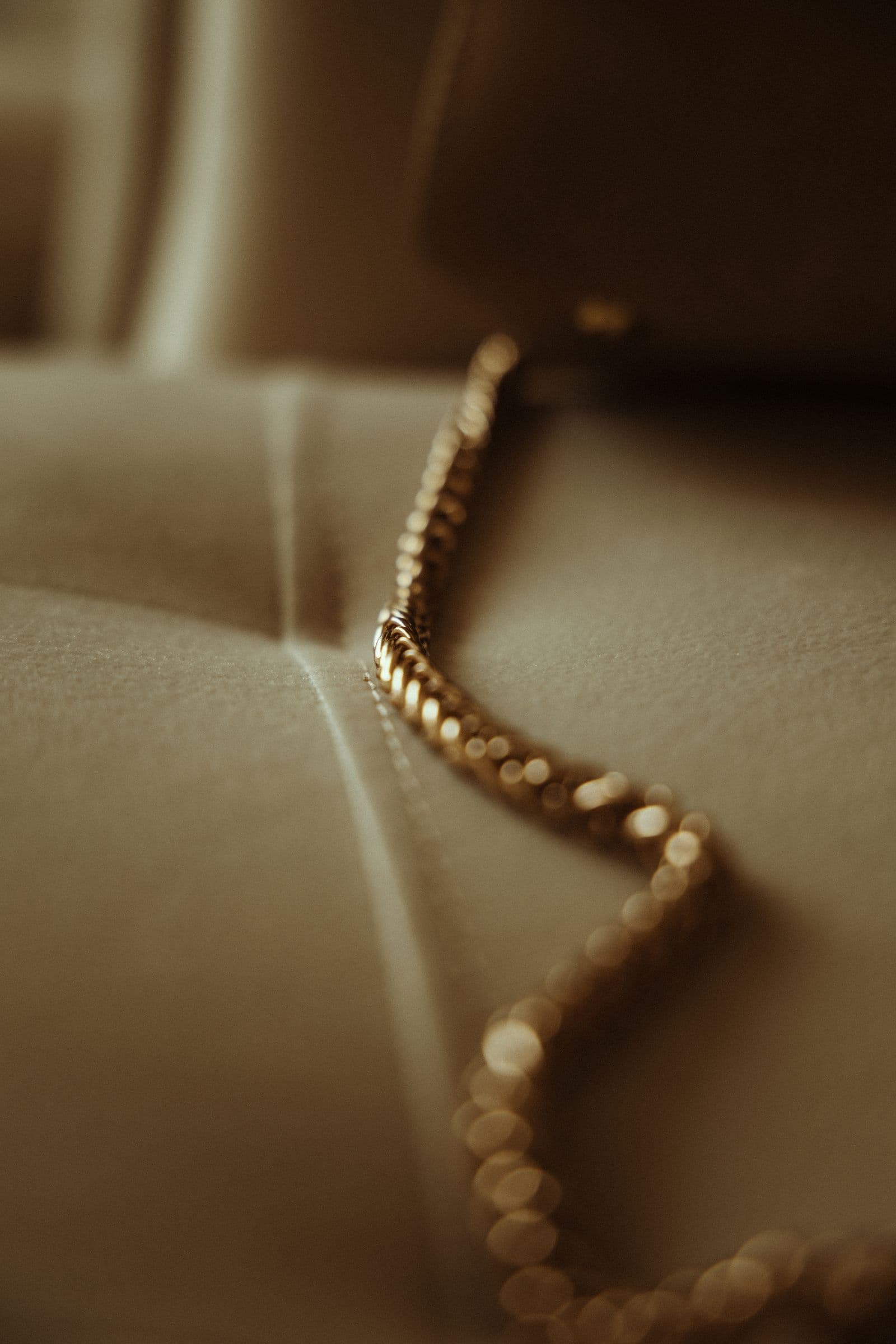 Close detail of a fine gold chain catching the light, resting on cream fabric.